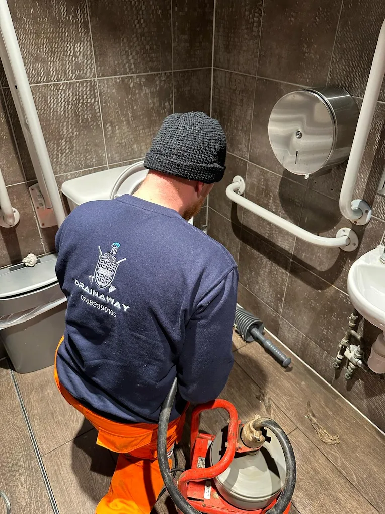 Reece clearing a blocked toilet in a commercial washroom, with a flex shaft machine set up beside him