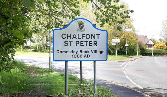 The Chalfont St Peter village sign at the roadside, reading 'Domesday Book Village 1086 AD'.
