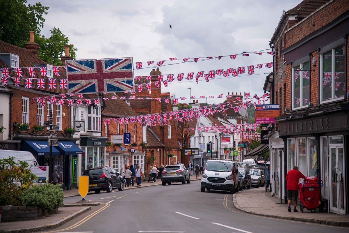 Marlow High Street dressed with Union Jack bunting, shops and parked cars either side.