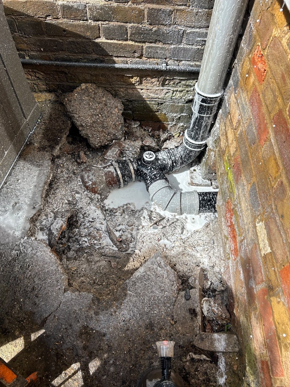 The same corner washed down with detergent, suds still on the ground and the pipework clean.