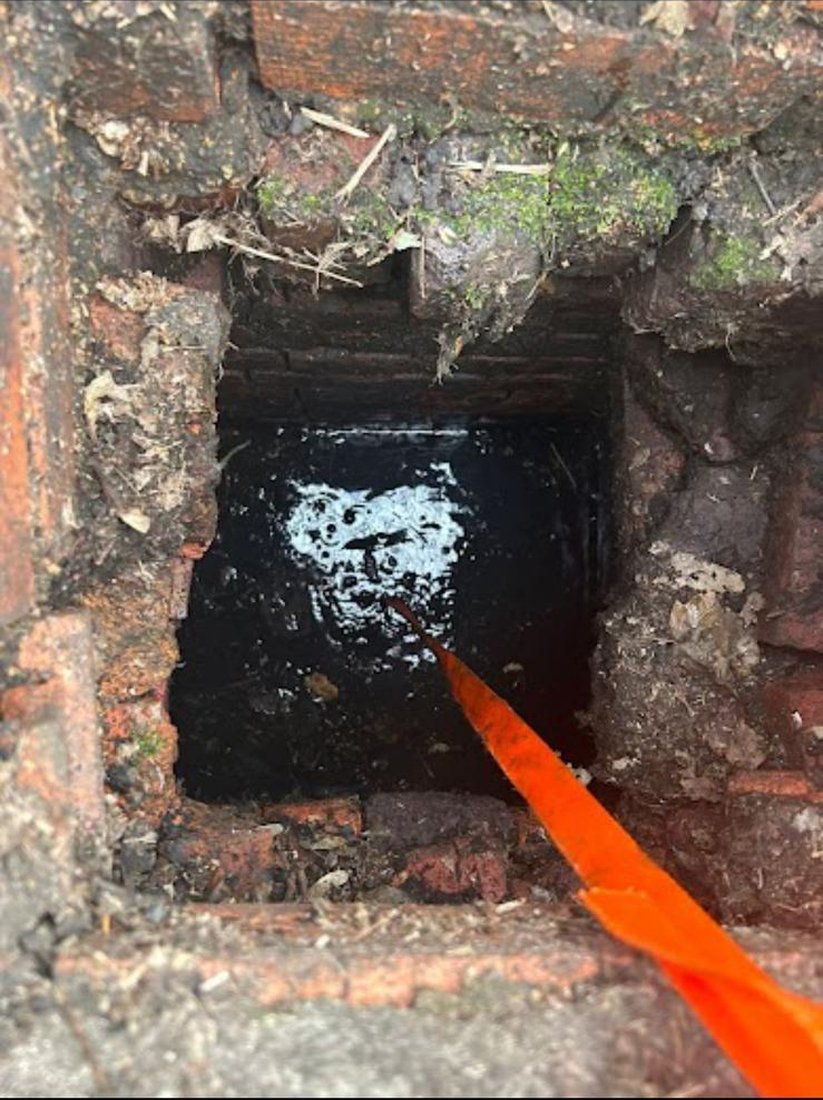 An orange retrieval strap lowered into a dark, water-filled roadside gully, feeling for a dropped set of keys.
