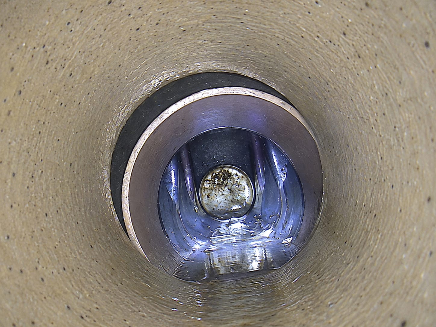 CCTV still looking along a clay drain to a damaged, open joint part way down the run, with a dark void behind the broken pipe wall.