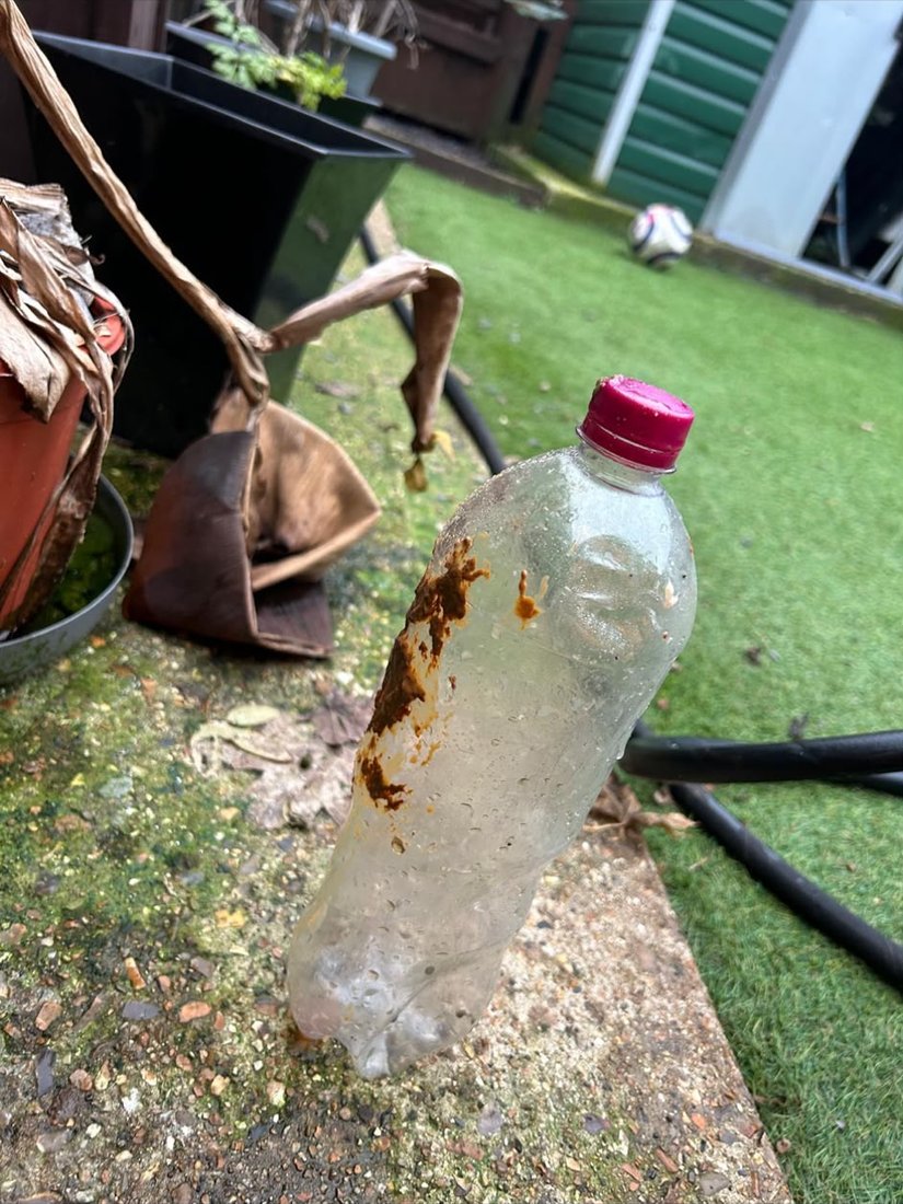 A plastic drinks bottle recovered from a drain, stood on a garden path with fat still smeared down one side.