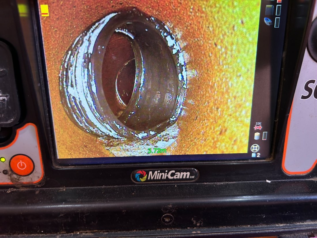 A CCTV drain survey monitor showing the inside of a pipe at a joint with visible scale