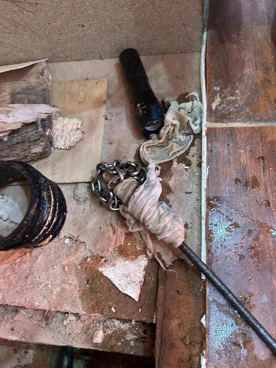 A lifted cellar floor with an old cast iron pipe collar, a torch, and rag pulled out of the drain on the rods.