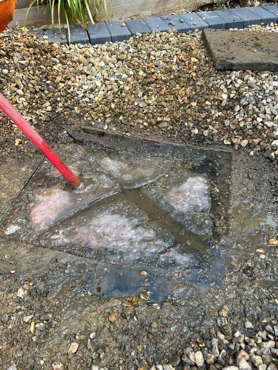 A chamber lid set in a gravel bed with dirty water and foam welling up around its edges.