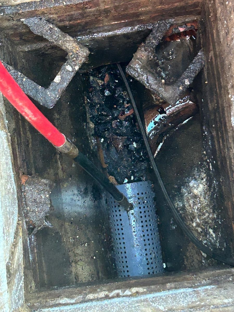 Inside a chamber with a perforated silt basket in the outlet and heavy black grease across the benching, a jetting hose fed in alongside.