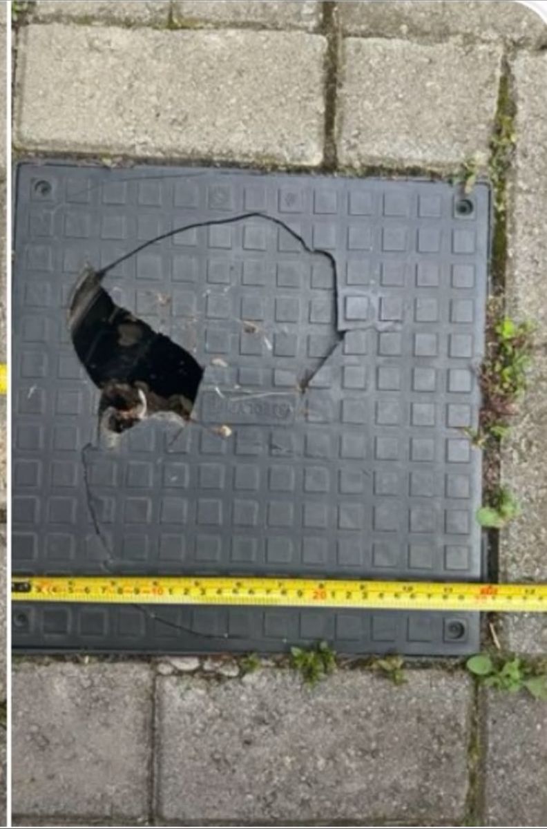 A plastic inspection chamber cover cracked right through with a hole punched out of it, a tape measure laid across for scale.