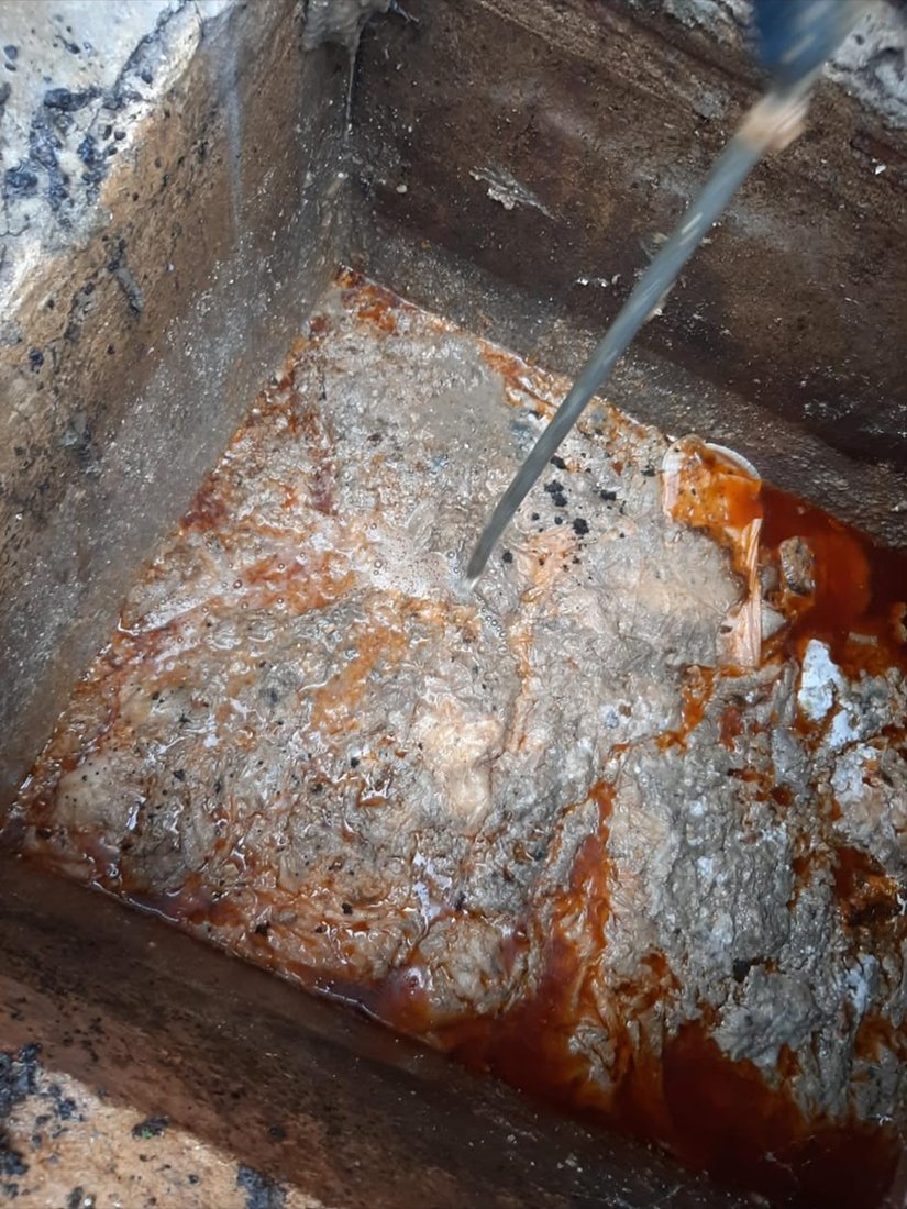 A chamber floor thick with congealed orange fat, being broken up under a jet of water.
