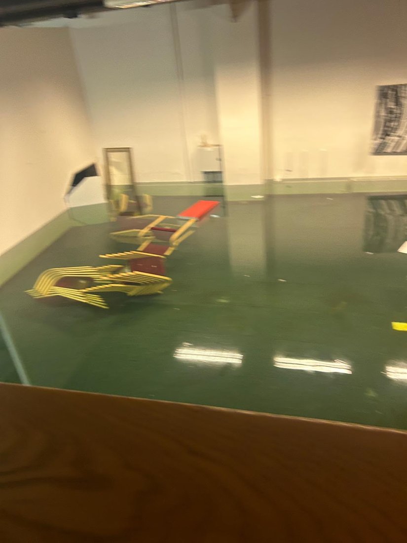 A function room flooded across its whole floor, with stacked chairs standing in the water.