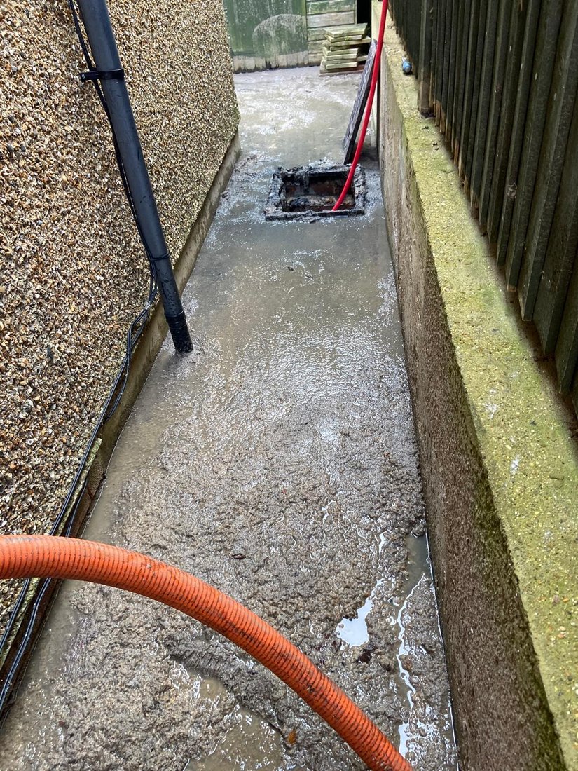 A narrow side passage flooded and silted over, with a gully part way along it and a suction hose run down to it.