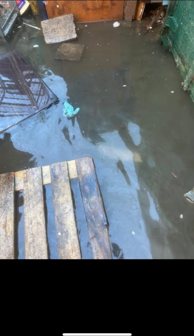 A service yard under dirty standing water, with pallets, bins and debris half submerged across it.