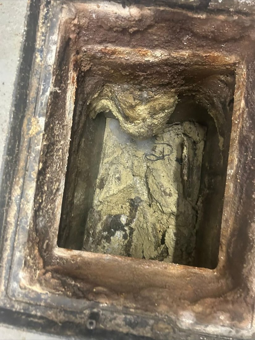 An open cast iron access chamber with the pipe below packed solid with pale congealed grease and fat.