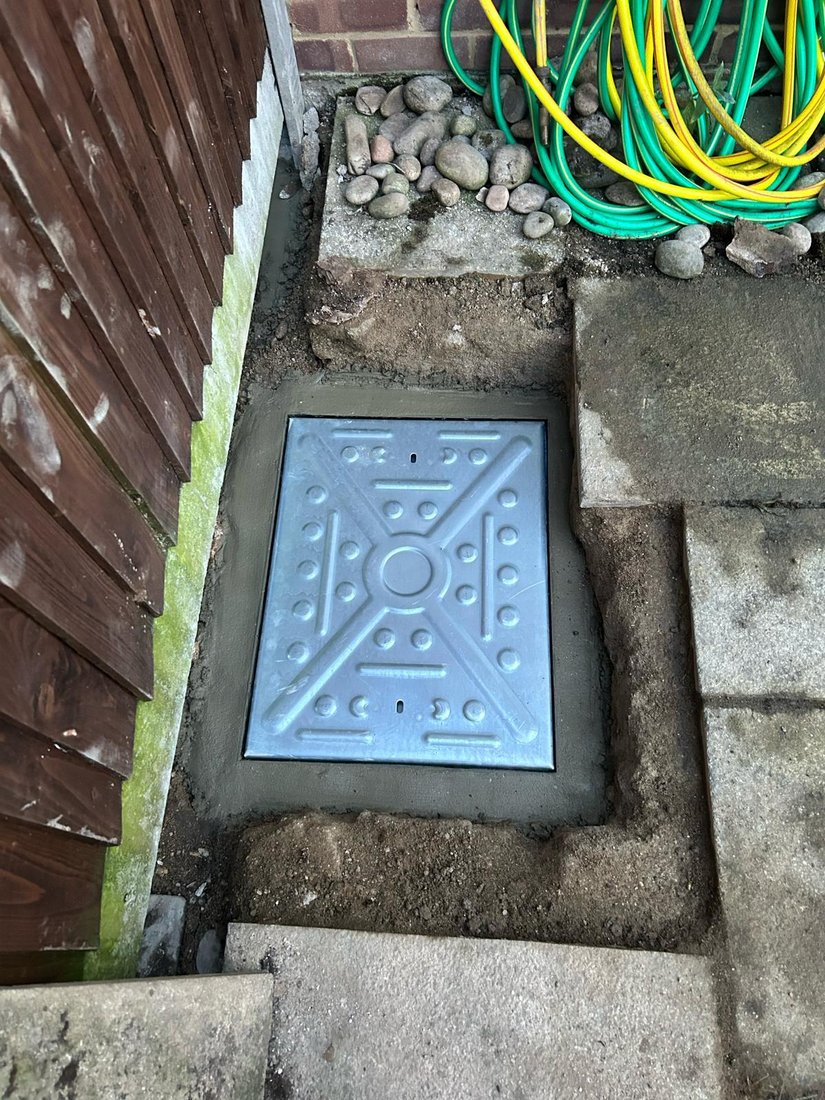A new steel inspection cover bedded into fresh mortar in a paved side passage.