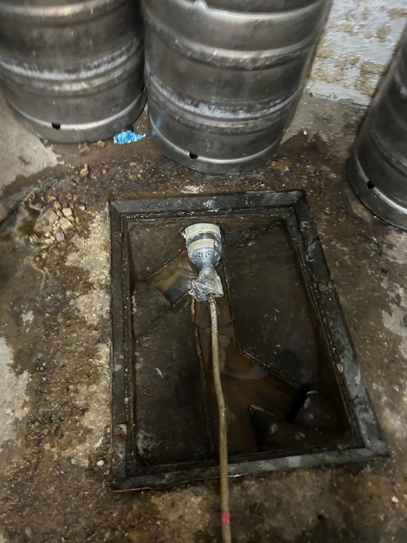 A resin patch liner on its packer being fed into an open drain chamber in a pub cellar, beer kegs standing behind it.