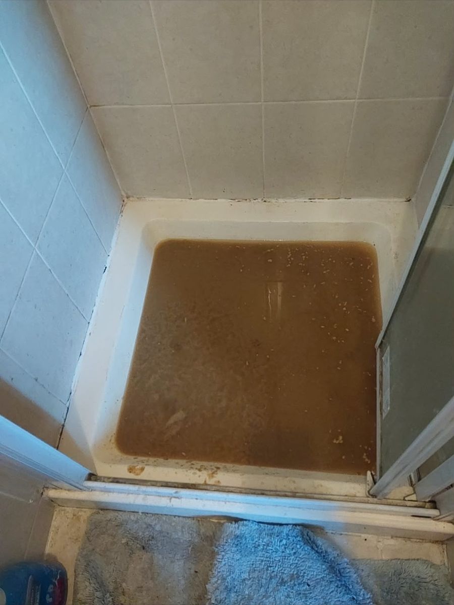 A tiled shower cubicle with the tray standing full of dirty brown water that is not draining away.