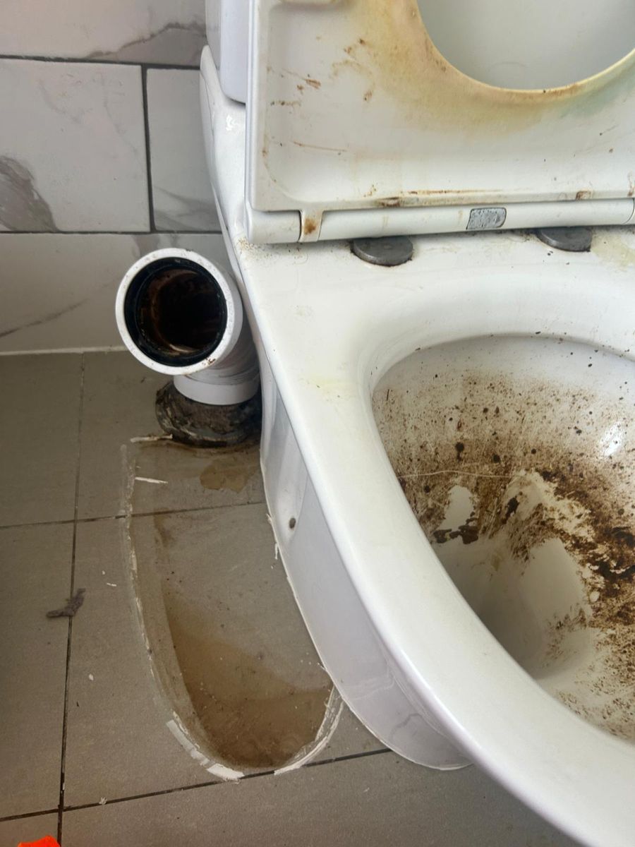 A toilet pulled off its soil pipe, leaving the open stub against the wall and brown water across the tiled floor.