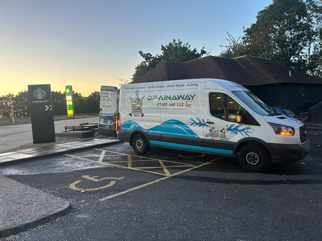 A liveried DrainAway van parked at a service station forecourt at dusk, signwritten with blockage clearance, hydro jetting, drain repair and lining.