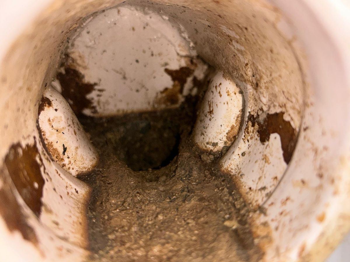A close-up down a white waste pipe, the bore narrowed to a small opening by grey-brown build-up on the walls.